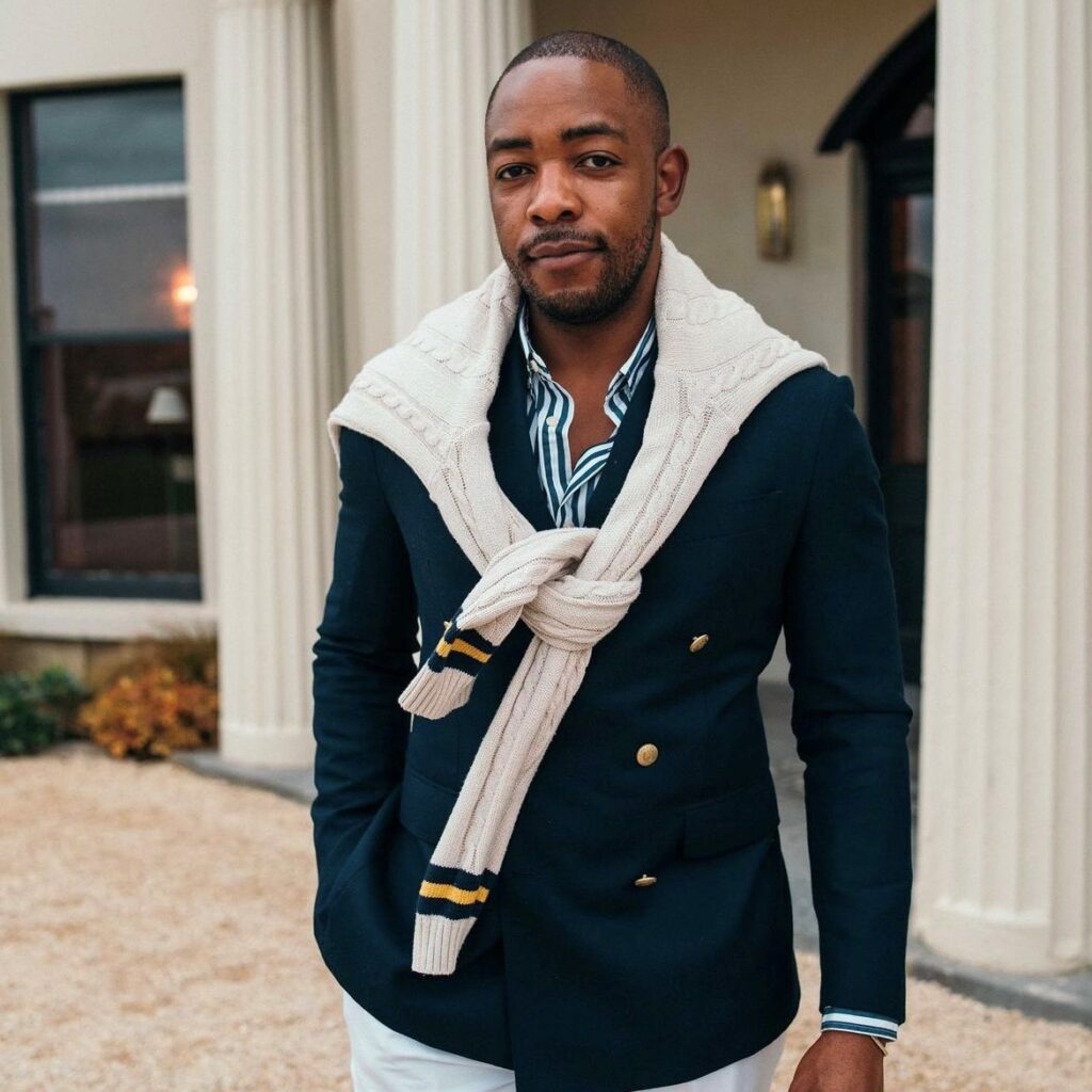 man wearing a navy blazer, striped button down and sweater over his shoulders