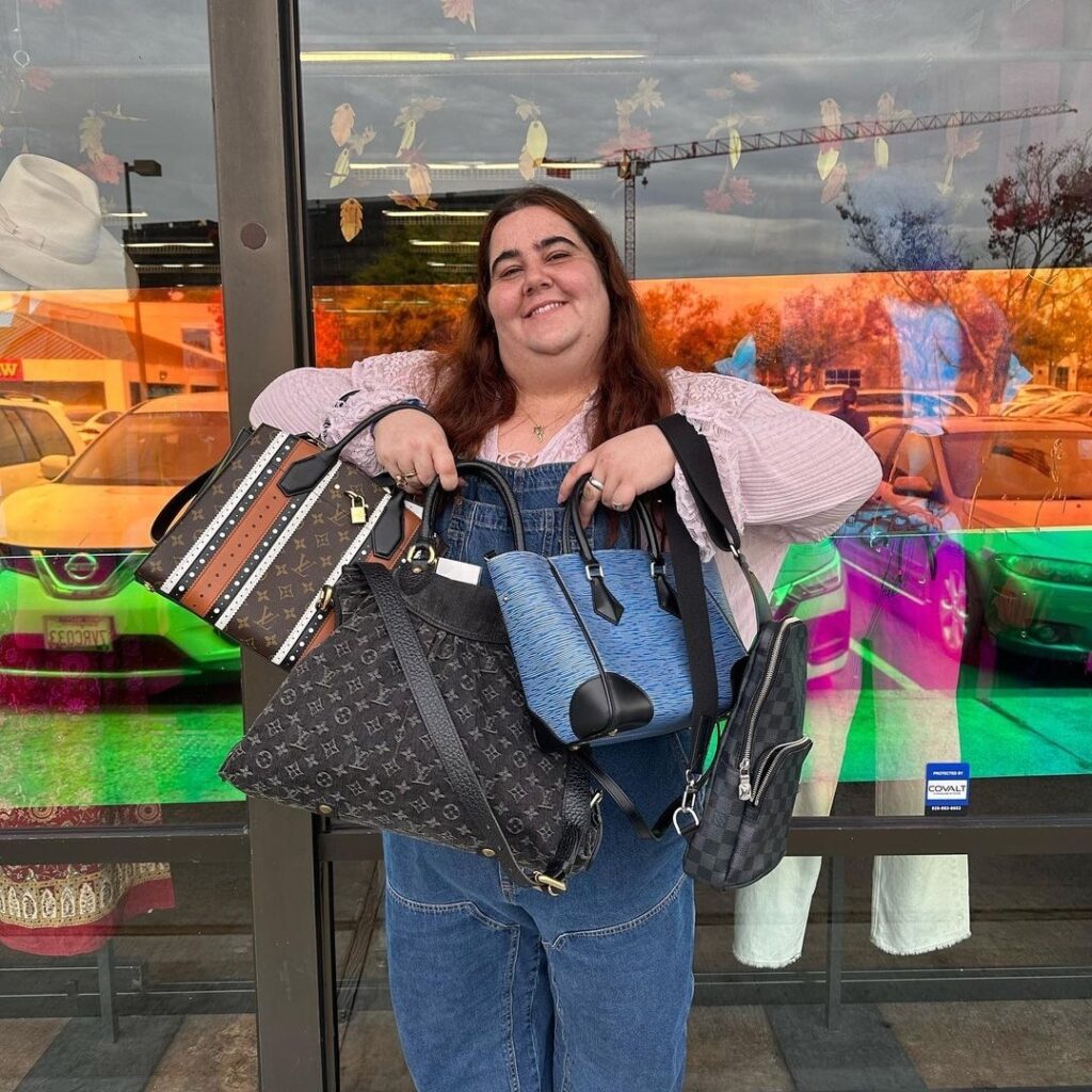 employee holding multiple designer handbags in front of one of the best places to thrift: Crossroads Trading