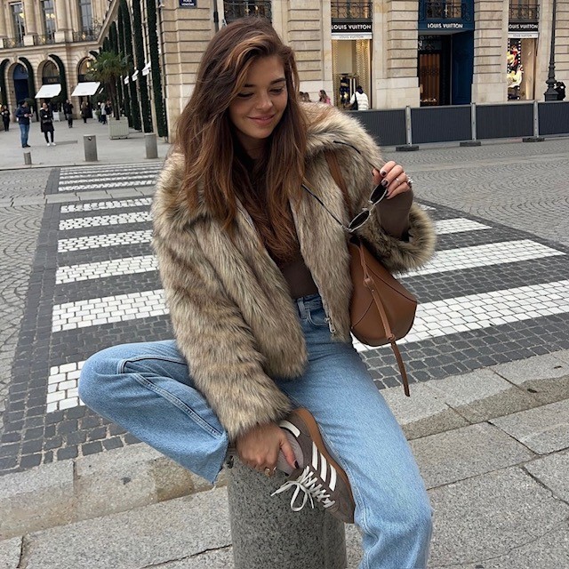 woman wearing a cropped beige jacket with jeans and sneakers