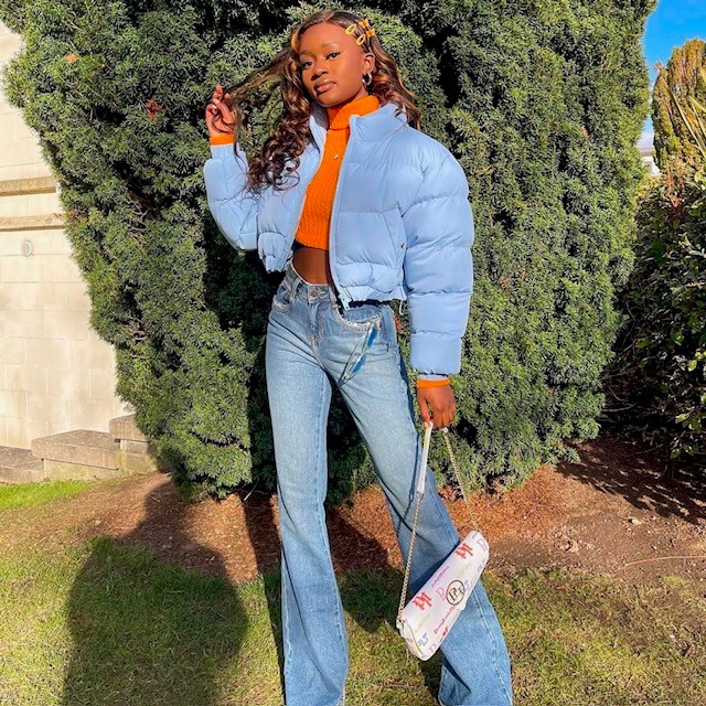 example of puffers: woman wearing a cropped baby blue puffer jacket with cropped orange top and high-waist jeans