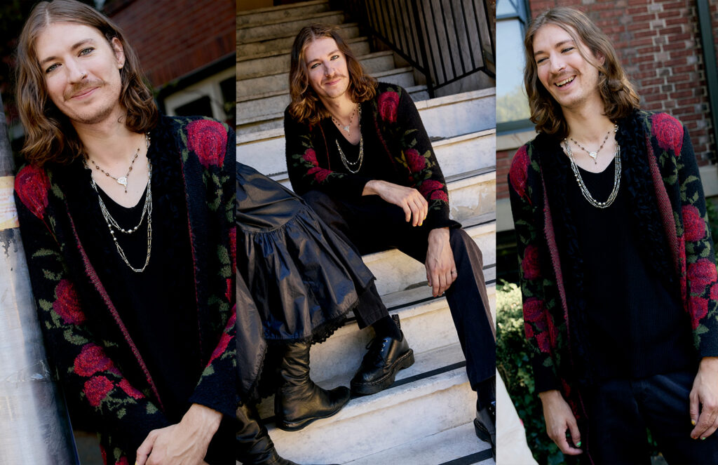 Aleks wearing a black and red rose printed cardigan, black shirt and pants, and doc marten oxford shoes