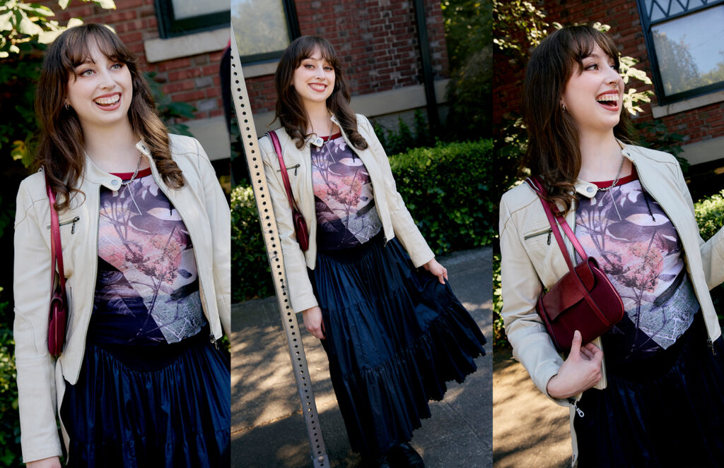 Claire wearing a white leather jacket with a red mesh printed shirt, navy midi skirt and black tall boots holding a maroon purse