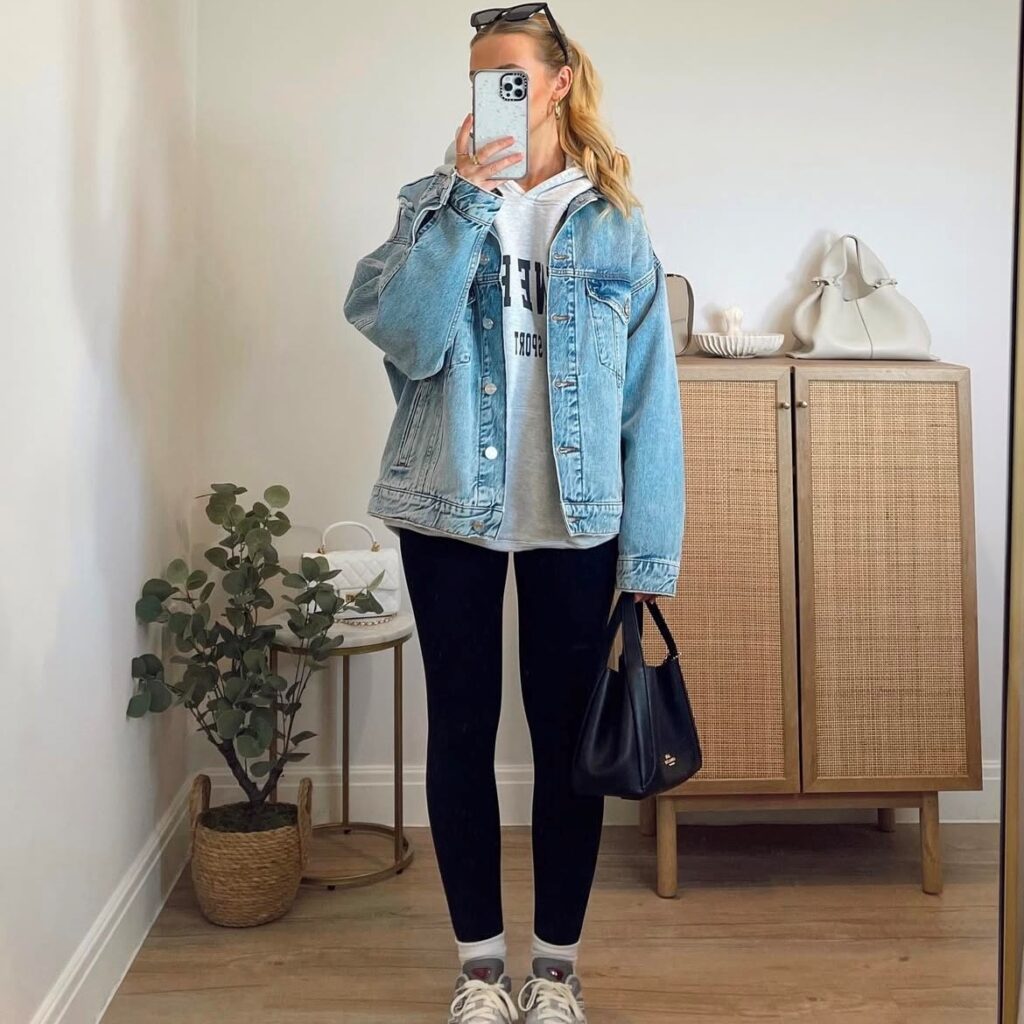 woman taking a selfie in a denim jacket, hoodie, and black leggings