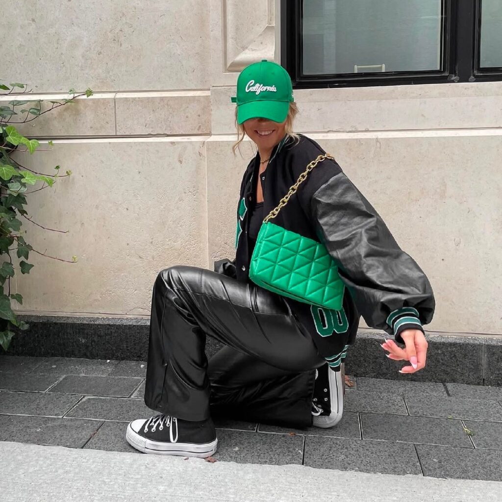 person with black pair, varsity jacket, and green cap