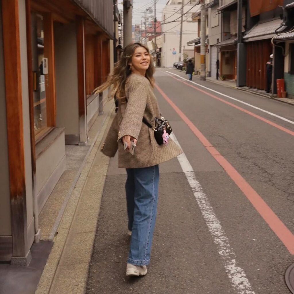 woman in brown tweed jacket, jeans, and trainers