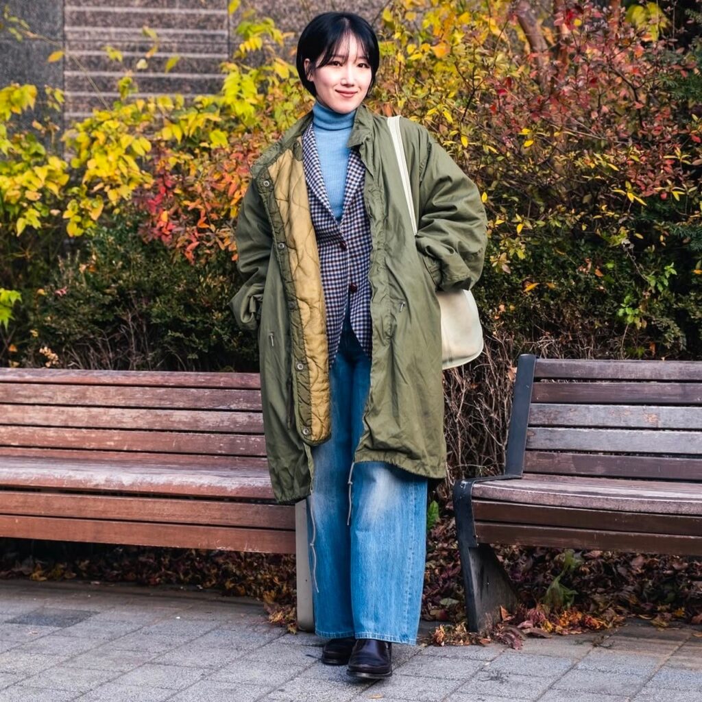 woman in checked blazer layered over a turtleneck and denim and under an army green windbreaker