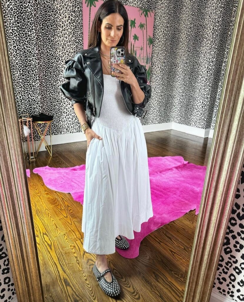 woman taking a selfie in a white drop waist dress with black leather jacket