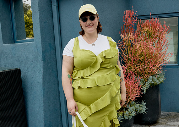 Daisy wearing a green ruffled dress, white t-shirt under, yellow dad cap and dark sunglasses