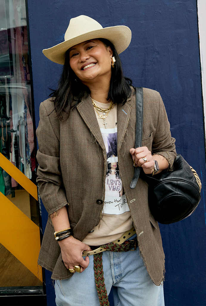 Lia wearing a cream cowboy hat, brown blazer, graphic tee, and blue denim shorts