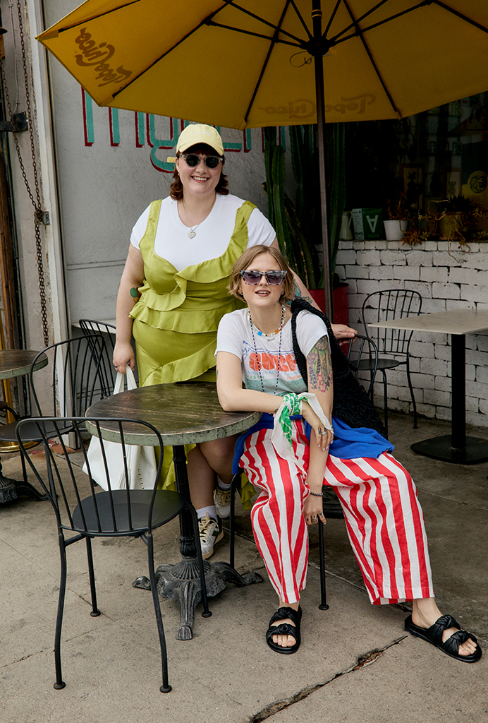 Daisy and Britt posing together in summer fashions at a table under a yellow umbrella