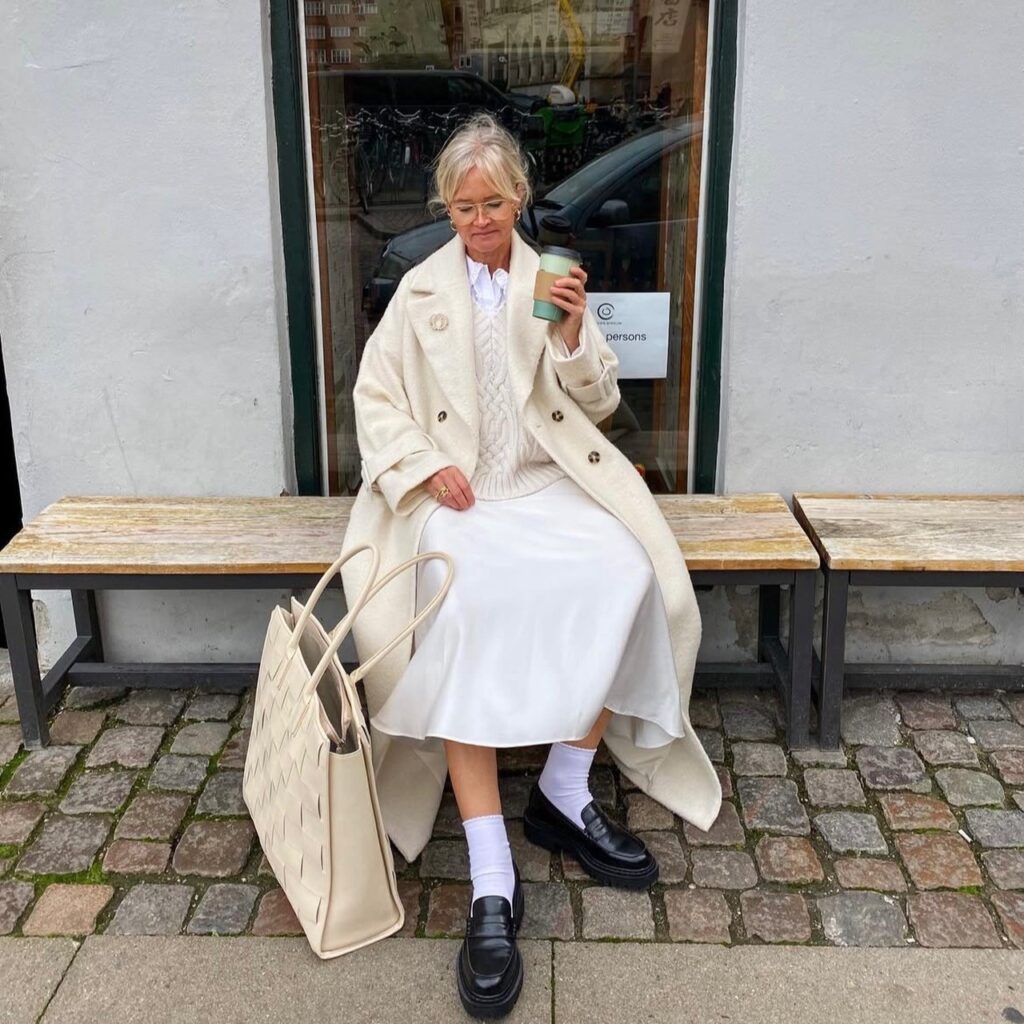 woman sitting on bench wearing a cream-colored outfit, white ankle socks, and black chunky shoes