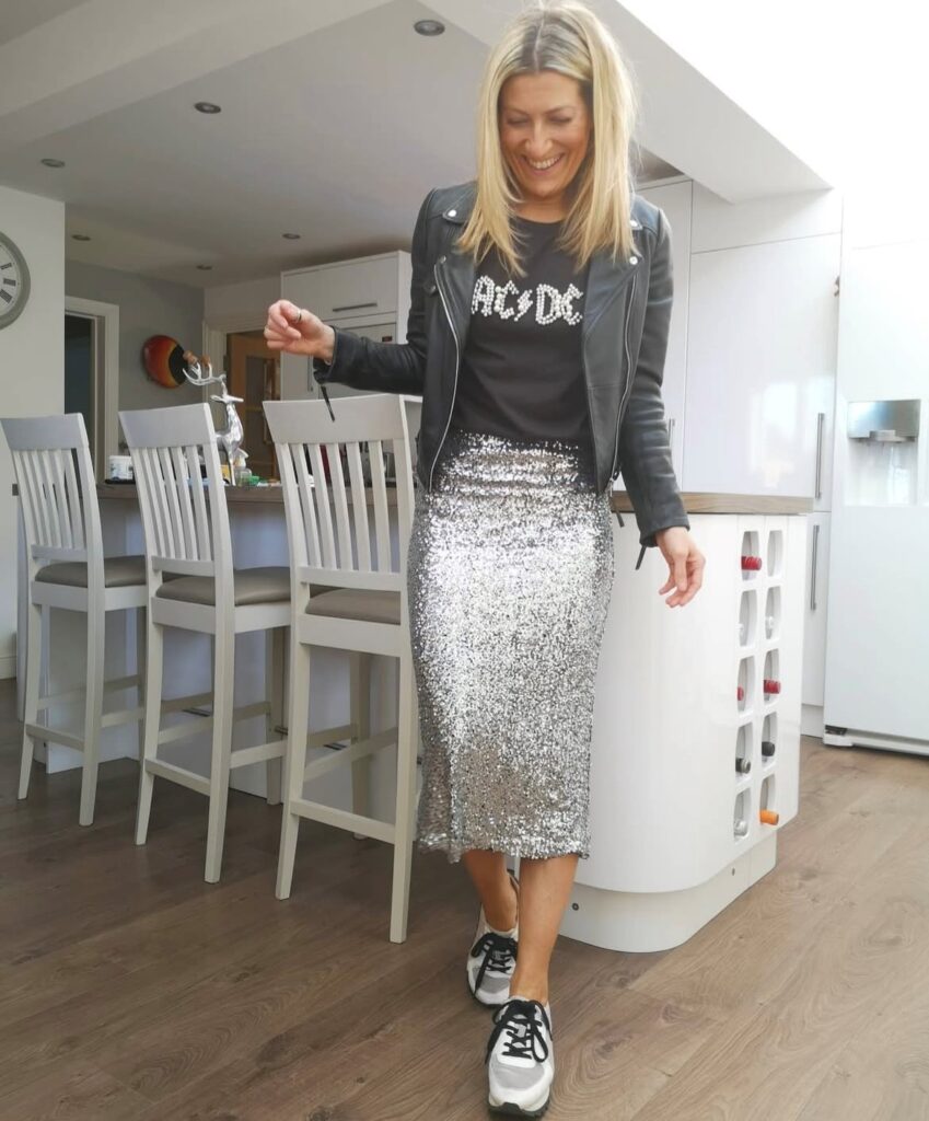 woman in black t-shirt with black leather jacket, silver sequin skirt, and trainers