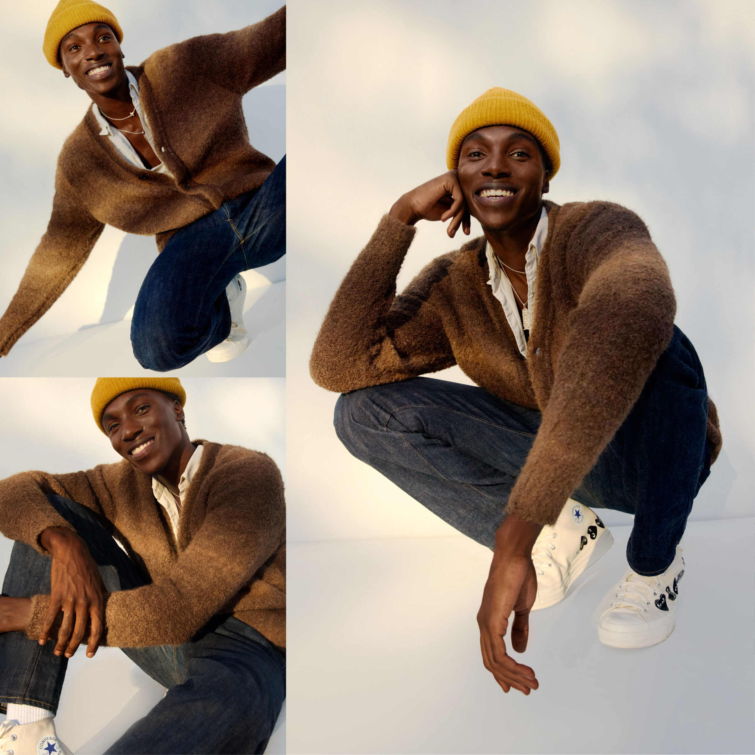 Male model wearing a brown gradient knit sweater over a white button down and dark denim jeans, shoes are white converse with two black hearts on the side and a yellow beanie