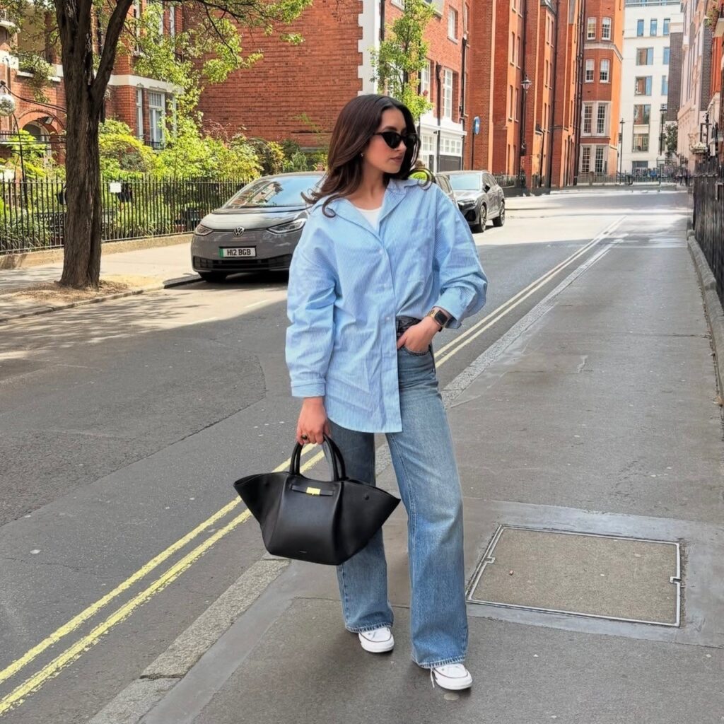 woman in an oversized button-up, jeans, sneakers, and designer handbag