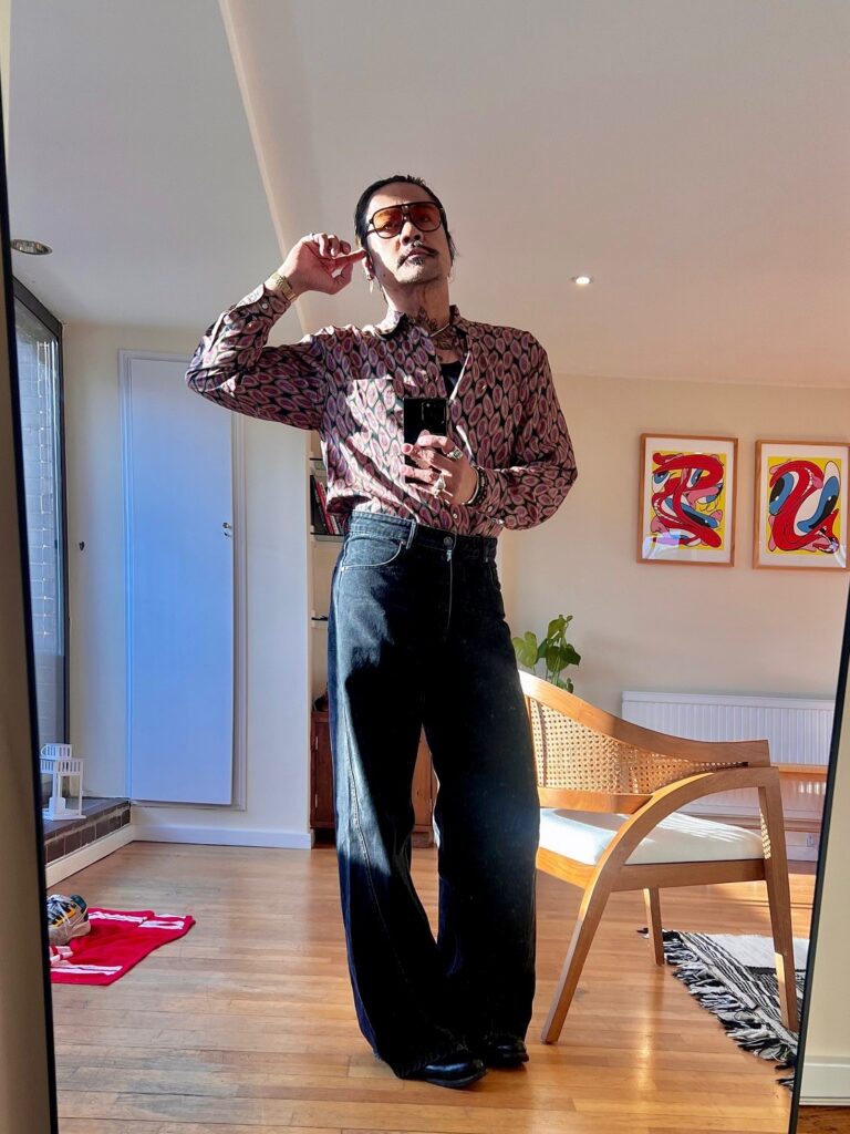 Arnel in a patterned button-up with dark denim jeans and large sunglasses