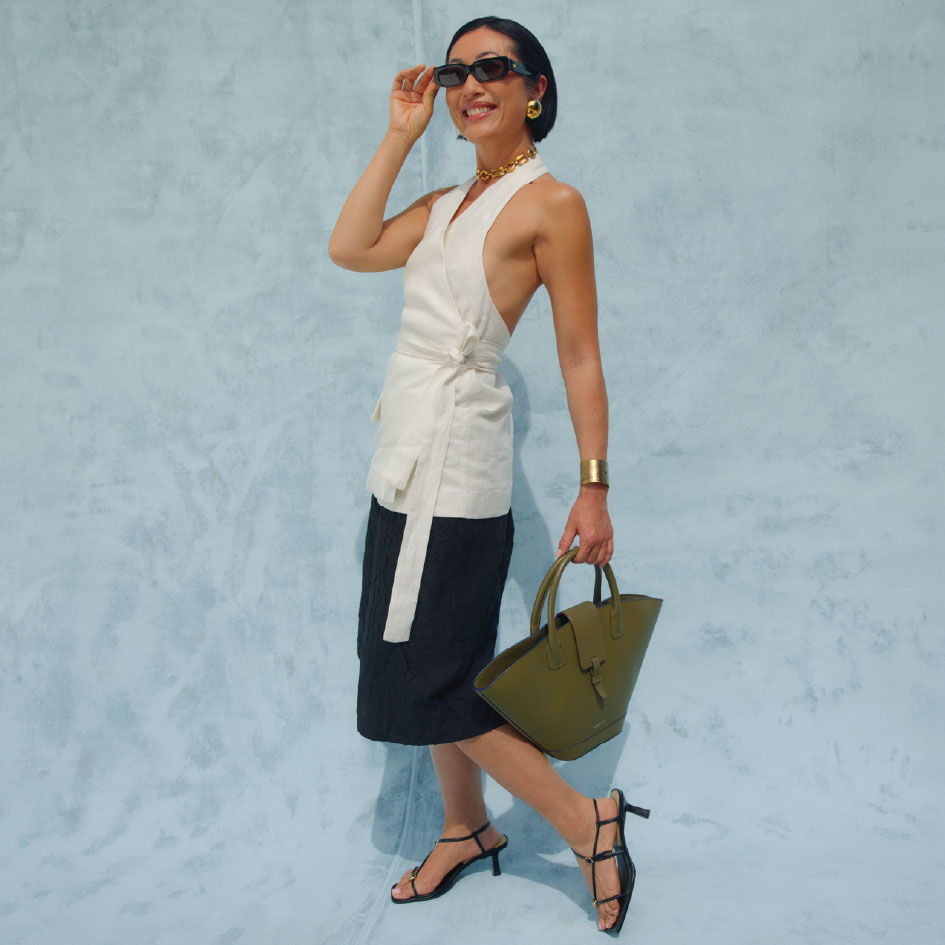 model wearing a white linen top, long black shorts, black low heels and a green handbag