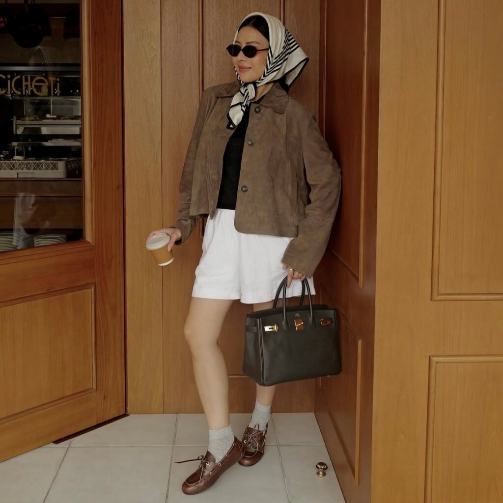 woman in shorts and suede jacket with head scarf and structured handbag