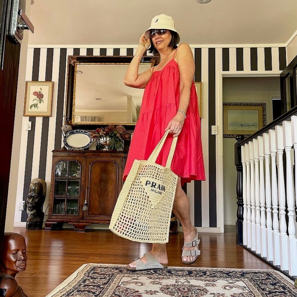Woman wearing red sundress with net bag and Birkenstocks.