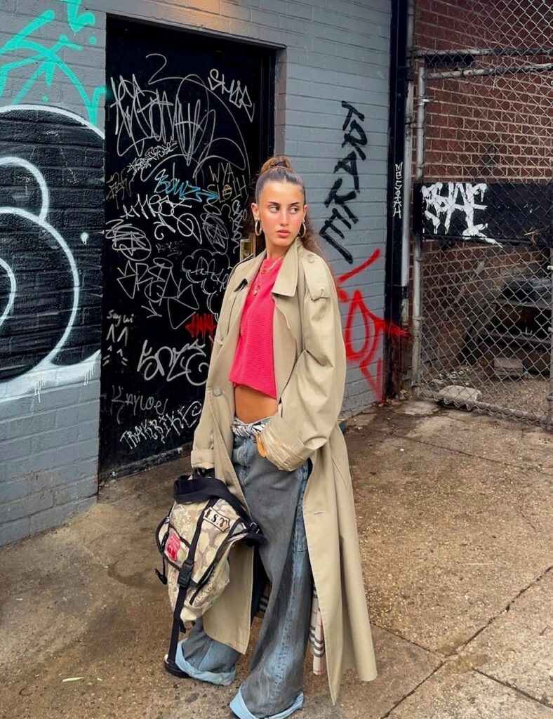 woman in oversized jeans, pink tee, and trench coat